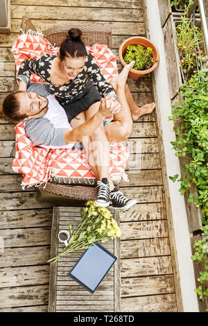 Junges Paar sitzen auf ihrem Balkon im Sommer halten sich an den Händen Stockfoto
