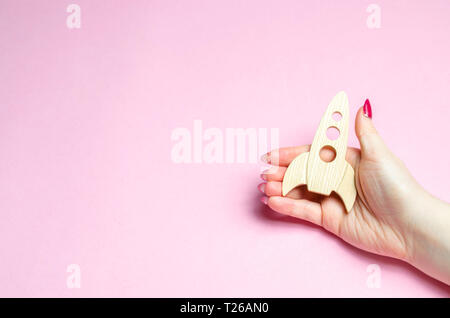 Frauen Hand mit einem Holz- Rakete auf einem rosa Hintergrund. Das Konzept der Verbesserung der Unternehmensleistung und Gewinnwachstum. Die Popularisierung der beliebten sc Stockfoto