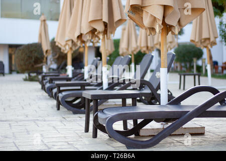 Eine Anzahl von leeren Strand Liegestühle am Pool unter Sonnenschirmen. Sonnenliegen, so dass in der Perspektive. Liegestühle, bereit, einen Rest zu nehmen Stockfoto