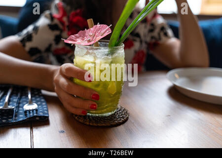 Frau mit tropischem Grün Farbe Cocktail in einem transparenten Tiki style cocktail Glas Stockfoto