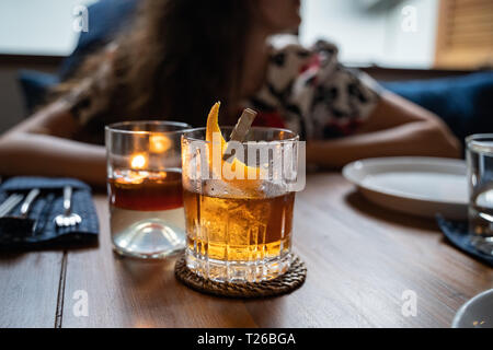 Old fashioned Cocktail in einem Whiskey Glas im Restaurant serviert. Frau in Soft Focus in den Boden zurück. Platz kopieren Stockfoto