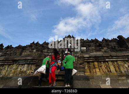 YOGJAKARTA, Indonesien - 08.23.2017. Nahaufnahme der touristischen trug ein rotes Kleid und zwei Reinigungskräfte in den Tempel Borobudur. Stockfoto