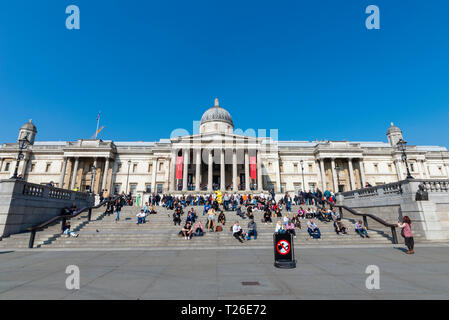 Das National Gallery Kunstmuseum und Treppen mit Touristen, Trafalgar Square, London, Großbritannien. Sonniger Tag mit blauem Himmel. Warm Stockfoto