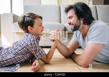 Ein Positives und Schönes Bild von Vater und Sohn auf dem Boden und halten einander die Hände. Sie spielen Stockfoto