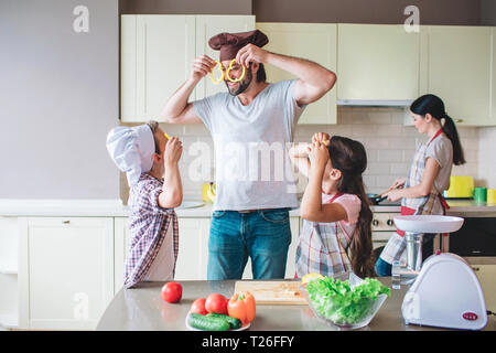 Lustig Mitglieder der Familie sind mit Essen spielen. Sie Stücke von gelbe Paprika um ihre Augen und lächeln. Frau steht hinter ihnen, und funktioniert. Sie i Stockfoto