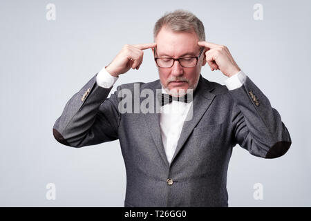 Älterer Mann in Anzug und Brille hält Finger auf Tempel, versuchen zu erinnern Idee generieren oder Stockfoto