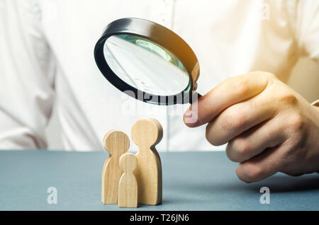 Eine Person, die sich mit Familie Zahlen durch ein Vergrößerungsglas. Die Studie der Familienzusammensetzung, Statistiken. Geburtenkontrolle und Kinder Polizei. Die Studie Stockfoto