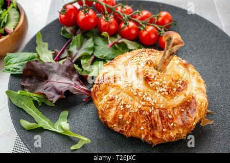 Huhn drumstick in der Teig im Ofen gebacken mit Kartoffeln, Tomaten, Zwiebeln und Gewürzen mit Beilage von Tomaten und grüner Salat. Stockfoto