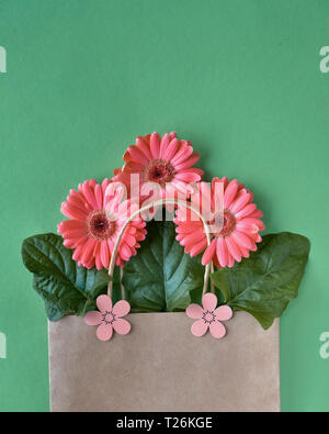 Coral Gerbera daisy flowers und Handwerk papper Einkaufstaschen auf grünem Papier Hintergrund, Frühling Verkauf Konzept Bild mit copy-Raum Stockfoto