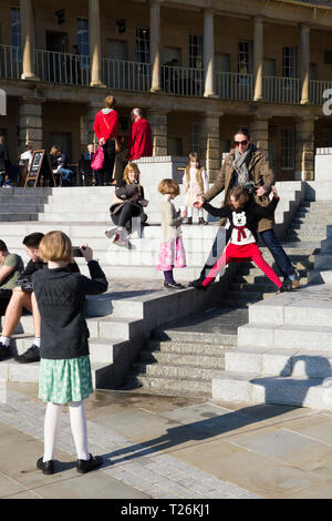 Kind spielt um das Wasserspiel & Besucher/Touristen sitzen und auf den Stufen im Viereck des wiederhergestellten Piece Hall entspannen. Sonnigen Tag/sun. Halifax. England UK. Der Tag war ein außergewöhnlich heißer Tag im Winter. Stockfoto