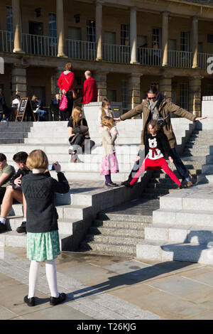 Kind spielt um das Wasserspiel & Besucher/Touristen sitzen und auf den Stufen im Viereck des wiederhergestellten Piece Hall entspannen. Sonnigen Tag/sun. Halifax. England UK. Der Tag war ein außergewöhnlich heißer Tag im Winter. Stockfoto