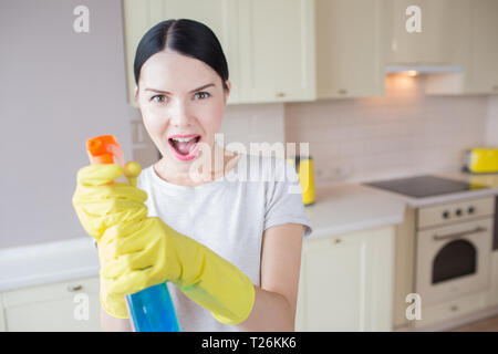 Ein Bild der aufgeregten Frau steht und hält blau Spray in den Händen. Sie zielt es auf die Kamera. Mädchen steht in der Küche Stockfoto