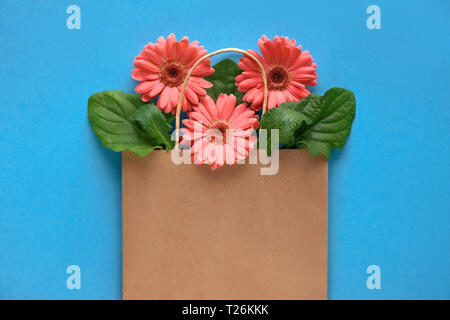 Coral Gerbera daisy flowers in Handwerk papper Shopping Bag auf blauem Papier Hintergrund, Frühling Verkauf Konzept Bild mit copy-Raum Stockfoto