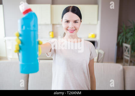 Ein Bild von brunette steht und zeigt Flasche mit blauer Flüssigkeit. Frau schaut auf Kamera und lächelt. Sie ist in der Mitte der Zimmer Stockfoto