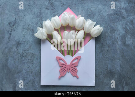 Frühling Flach, Weiße Tulpen in Weiß und Rosa Umschlag auf Grau strukturierten Hintergrund mit rosa Schmetterling Deko Stockfoto