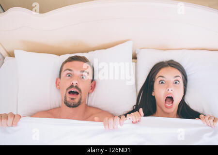 Und Sared terified Mann und eine Frau liegen im Bett. Sie bedeckt mit weißen Decke. Die Menschen halten es mit den Händen. Sie schauen direkt auf der Kamera Stockfoto