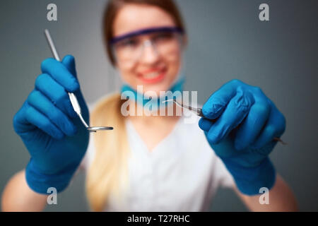 Freundliche nette junge Frau Zahnarzt suchen auf Kamera und Lächeln. Sie halten dental Tools. Auf grünem Hintergrund isoliert Stockfoto