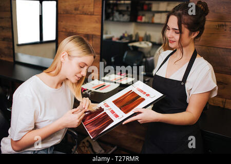 Junge schöne Frau und Friseur ihr blondes Haar Vergleich mit Farbe Haare von Palette vor der richtigen Färbung. Beauty, Haare färben Konzept Stockfoto