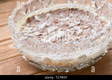 Machen Sie Mimosen, Fischsalat. Schicht von Konservenfischen. Kristallsalatschüssel auf Holzgrund. Stockfoto