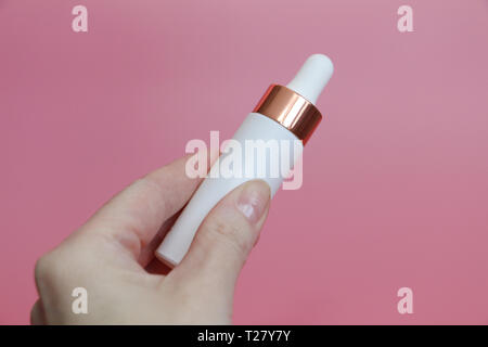 In der Hand einer Frau weiße Tube mit Flüssigkeit. Weibliche Hand hält weiße Flasche mit Elixir. Rosa Hintergrund. Stockfoto