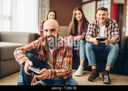 Lächelnd Freunde mit Joysticks spielt Tv-konsole zu Hause. Gruppe von Spielern mit joypads Videospiel spielen, männliche und weibliche Spieler mit Gamepads Stockfoto