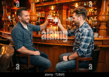 Zwei lächelnde männliche Freunde trinkt Bier an der Theke im Pub. Bärtige Männer mit Tassen Spaß in bar, gute Freunde Stockfoto