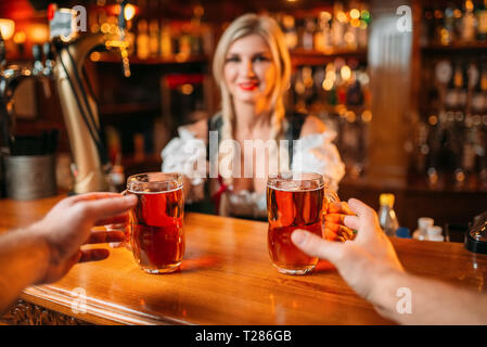 Zwei männliche Freunde nimmt Bier von Kellnerin an der Zähler im Pub. Männer mit Tassen Spaß in bar Bardame in traditionellen Retro Stil Stockfoto