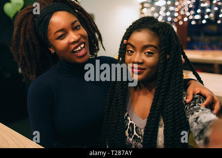 Zwei junge afrikanische Modelle schauen gerade und Pose. Sie lächeln und sitzen zusammen im Café Stockfoto