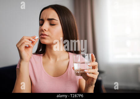 Junge Frau halten weiße Pille in der Hand. Sie wird es zu essen. Modell Glas waterin Hand. Sie sieht traurig und depressiv Stockfoto