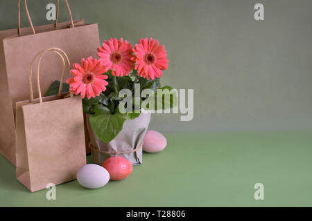 Coral Gerbera daisy flowers, Handwerk papper Einkaufstaschen und Ostern Eier auf grünem Papier Hintergrund. Frühling Verkauf Konzept Bild mit copy-Raum Stockfoto