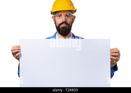 Gut aussehender bärtiger Mann builder Arbeiter im schützenden Bau gelben Helm Holding weiß Werbebanner mit Platz für Informationstext, Isola Stockfoto