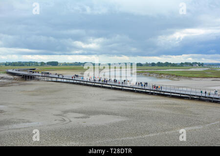 Brücke mit Touristen, die zu französischen historische Sehenswürdigkeiten attracktion Le Mont Saint Michel über das Wasser bei Ebbe an einem regnerischen Tag Stockfoto