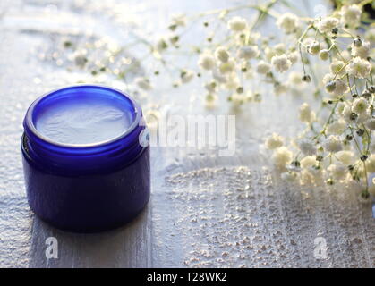 Ein blaues Glas Glas mit hausgemachten Bio Deo weiß Holz- Hintergrund mit kleinen weißen Blüten und Platz für Kopieren. Skin Care Produkte Konzept. Stockfoto