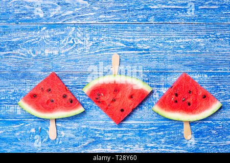 Scheibe frische Wassermelone auf einem Stock. Wassermelone ist in der Form eines Dreiecks schneiden. auf blauem Hintergrund Holz Stockfoto