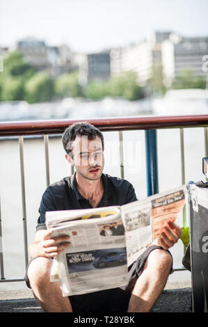 Ein Mann liest eine Zeitung im Sommer neben dem Fluss Themse in London. UK. Stockfoto