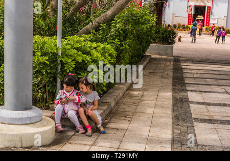 Zwei junge Mädchen zusammen zu sitzen, die sich in der Ecke der Wand, im Küstenort Stanley, Hong Kong Stockfoto