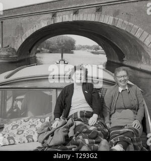 1950, historische, zwei glückliche Damen mit Teppichen auf Sie entspannen auf dem Deck eines Motors oder Cabin Cruiser starten entlang eines Flusses in Oxford, England, UK. Stockfoto