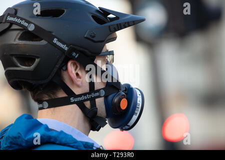 Radfahrer in London, UK, trägt einen Helm und eine Maske mit einem Filter über seine Nase und Mund beim Radfahren zu Hause nach der Arbeit festgeschnallt. Stockfoto