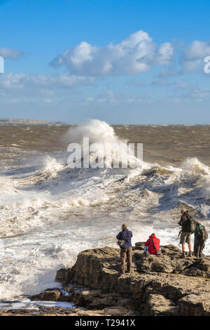 PORTHCAWL, WALES - Oktober 2018: Gruppe von Leuten auf den Felsen in Porthcawl, die Bilder von großen Wellen auf die Flut. Stockfoto