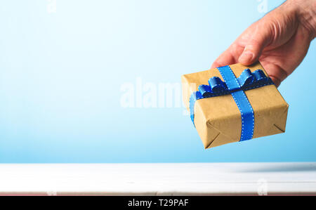 Geschenkbox in des Menschen Hand über blauen Hintergrund, Geschenk, Überraschung, Vatertag Konzept. Platz kopieren Stockfoto