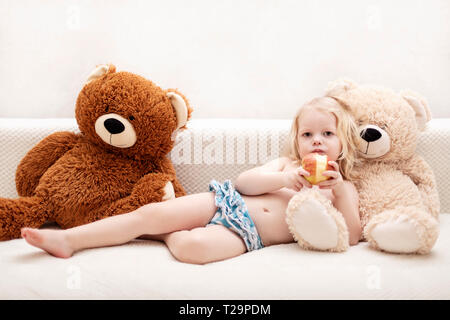 Kleiner Junge, drei Jahre alt, spielt und isst einen Apfel auf dem Sofa. Selektive konzentrieren. Stockfoto