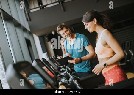 Junge Frau mit Trainer, auf Laufband im Fitnessstudio Stockfoto