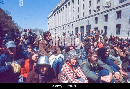 Während der 1971 Tag der Proteste gegen den Vietnamkrieg, eine große Anzahl von Warm gekleidete männliche und weibliche Demonstranten zusammen sitzen, an einem sonnigen Tag, auf dem Bürgersteig neben dem des US-Justizministeriums Gebäude (jetzt die Robert F. Kennedy Justizministerium Gebäude), in Washington, DC, Mai 1971. () Stockfoto