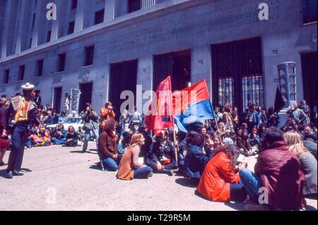 Während der 1971 Tag der Proteste gegen den Vietnamkrieg, einem großen Kreis von Warm gekleidete männliche und weibliche Demonstranten zusammen sitzen außerhalb des US-Justizministeriums Gebäude (jetzt die Robert F. Kennedy Justizministerium Gebäude) hält zwei Fahnen, darunter ein Rot, Blau und Gold Vietcong Flagge, in Washington, DC, Mai 1971. () Stockfoto