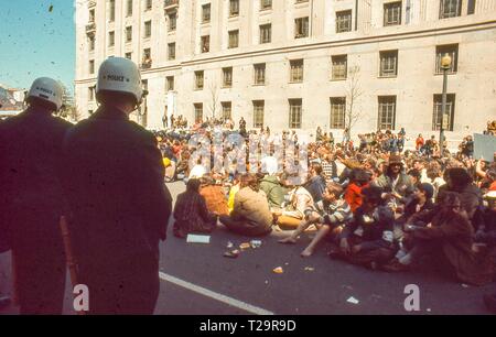 Während der 1971 Tag der Proteste gegen den Vietnamkrieg, eine Masse von Demonstranten in der Mitte des 10. ST NW, an einem sonnigen Tag; der Rücken von zwei ständigen Polizisten, das Tragen von Uniformen und White riot Helme, werden im linken Vordergrund sichtbar, in Washington, DC, Mai 1971. () Stockfoto