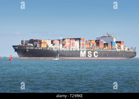 Das Containerschiff MSC ASYA, tritt in die Tiefen Wasser Kanal wie nähert sie sich der Hafen von Southampton, ein Segelboot vorbei Im Vordergrund, UK. Stockfoto