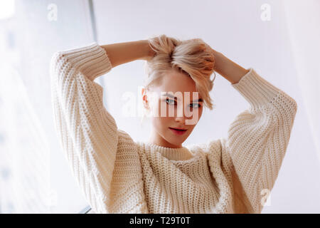 Frau beige Übergröße Pullover steht in der Nähe der Fenster Stockfoto