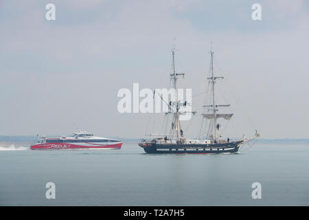 Die Ausbildung Schiff (Tall Ship), TS-ROYALISTISCHEN, Abfahrt im Hafen von Southampton, UK. Die Isle of Wight Fähre führt Hinter. 28. März 2019. Stockfoto