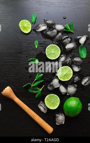 Limetten, Minze und Eiswürfel auf schwarzem Hintergrund. Zutaten für Mojito Cocktail. Ansicht von oben. Stockfoto