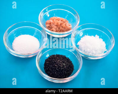 Kristallschalen mit Himalaya Salz, schwarz Hawaii Salz, Salz und Salz Flocken auf einem blauen Hintergrund Stockfoto